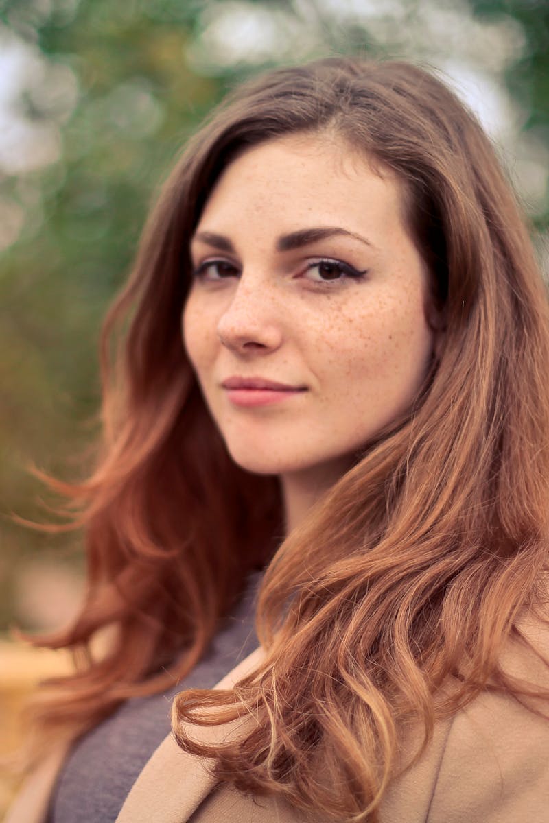 Home A young woman with long hair smiles confidently for an outdoor portrait session.